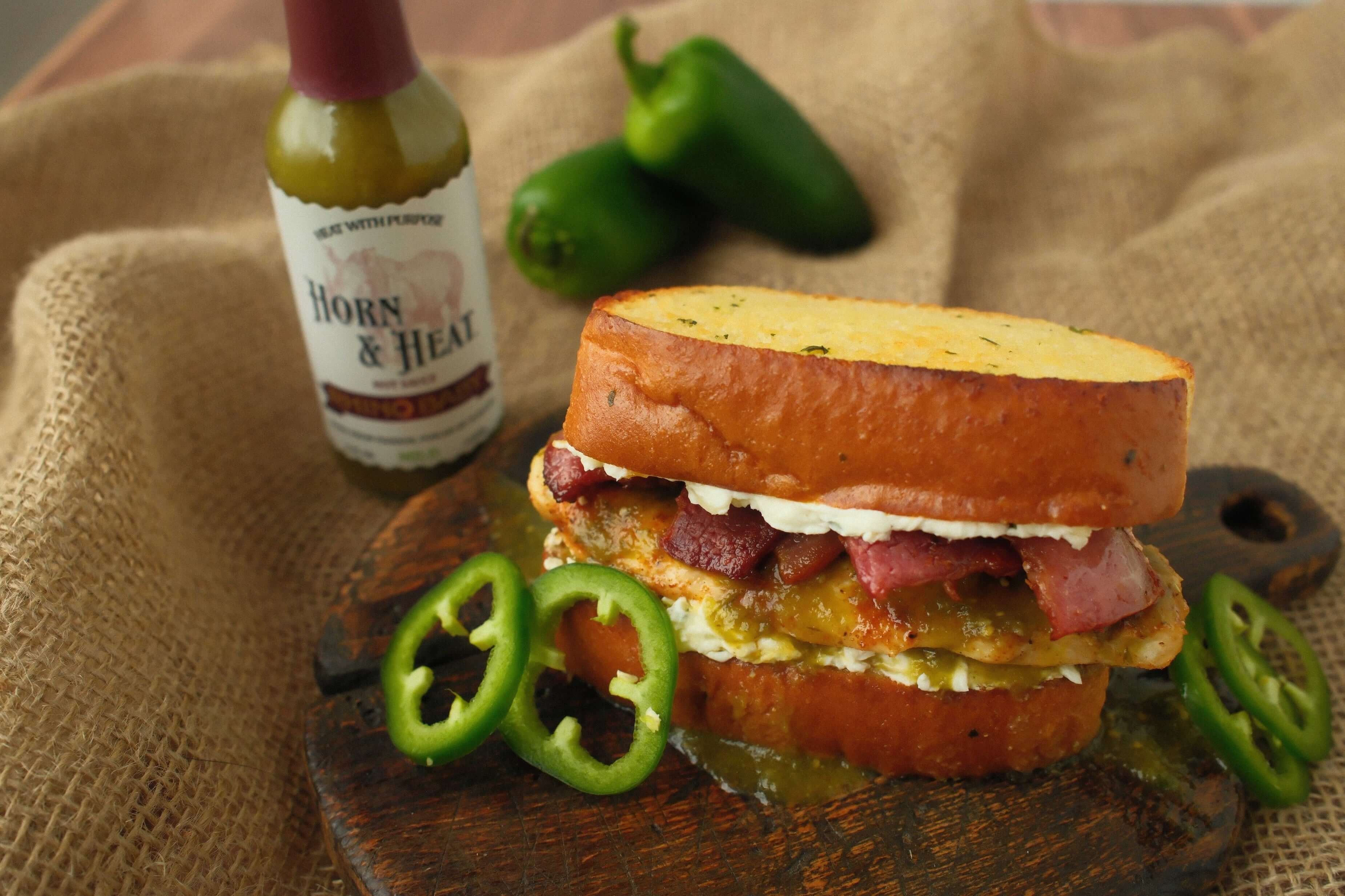 Delicious Jalapeño Popper Chicken Sandwich with jalapeño slices and sauce on a wooden board.