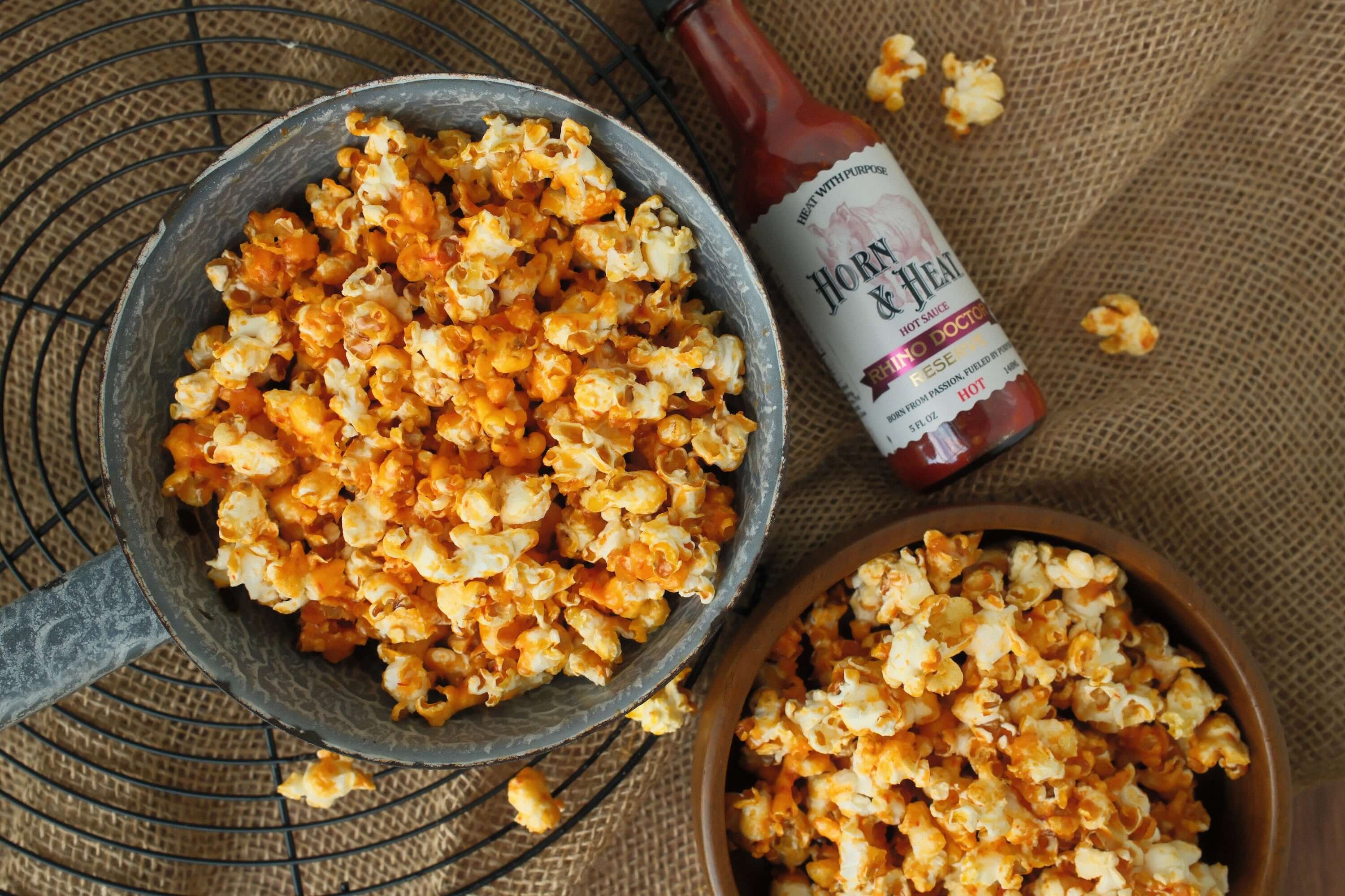 Horn & Heat Firehouse Popcorn in a rustic bowl with a bottle of Horn & Heat sauce