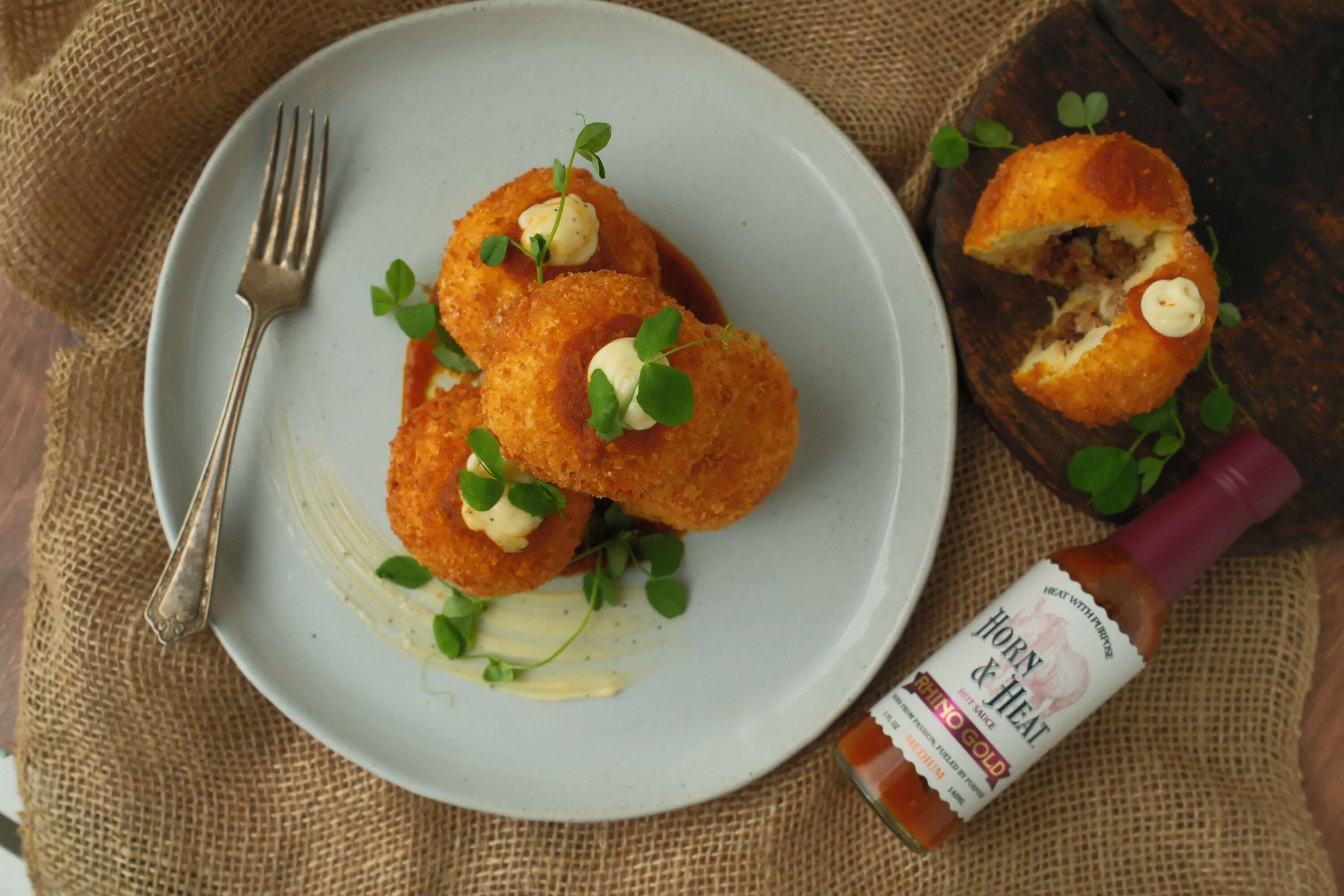Horn & Heat Spanish Bombas with Rhino Gold Hot Sauce served on a plate with garnish and a fork.