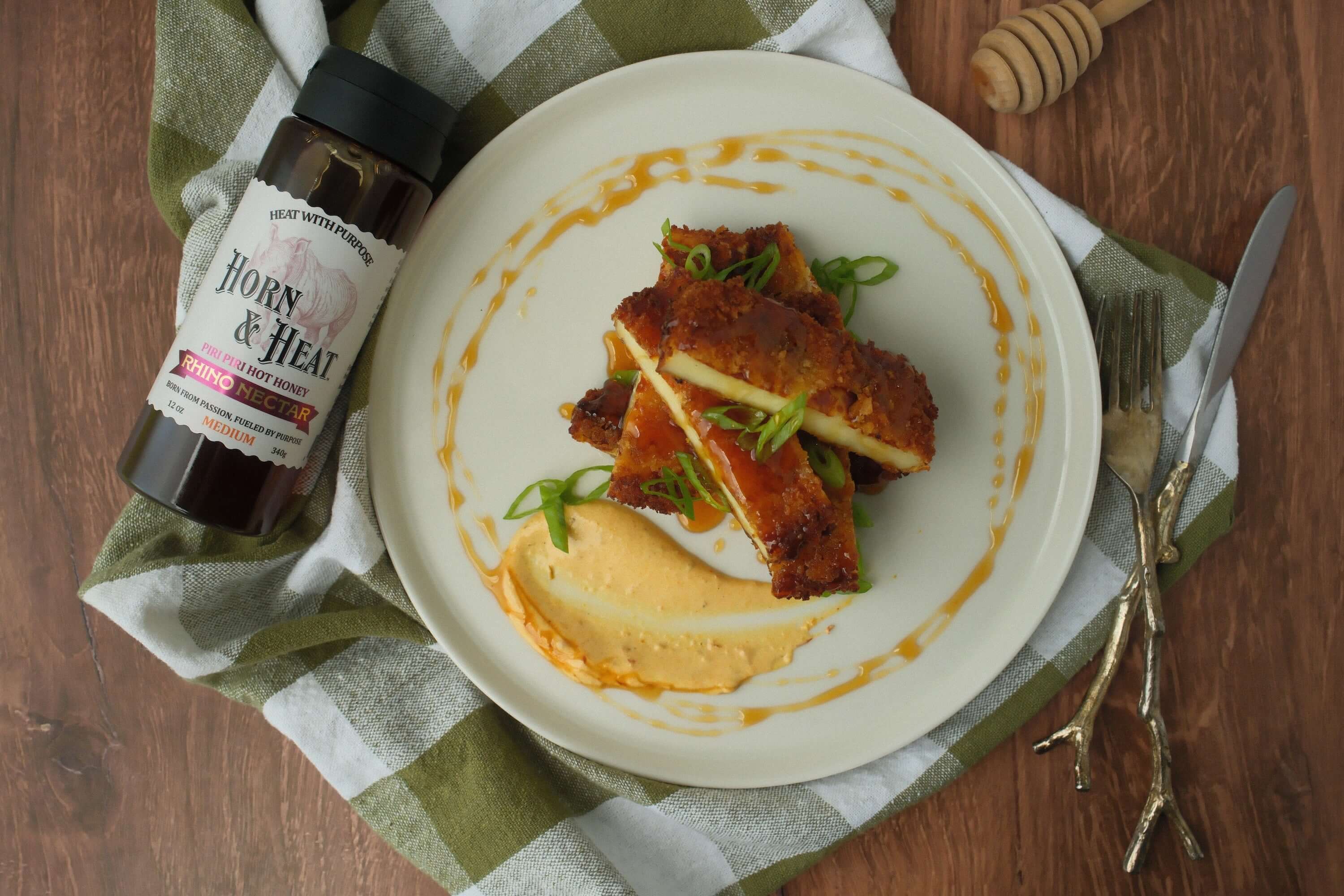 Crispy Halloumi with Rhino Nectar Hot Honey served on a plate with sauce and green onions.
