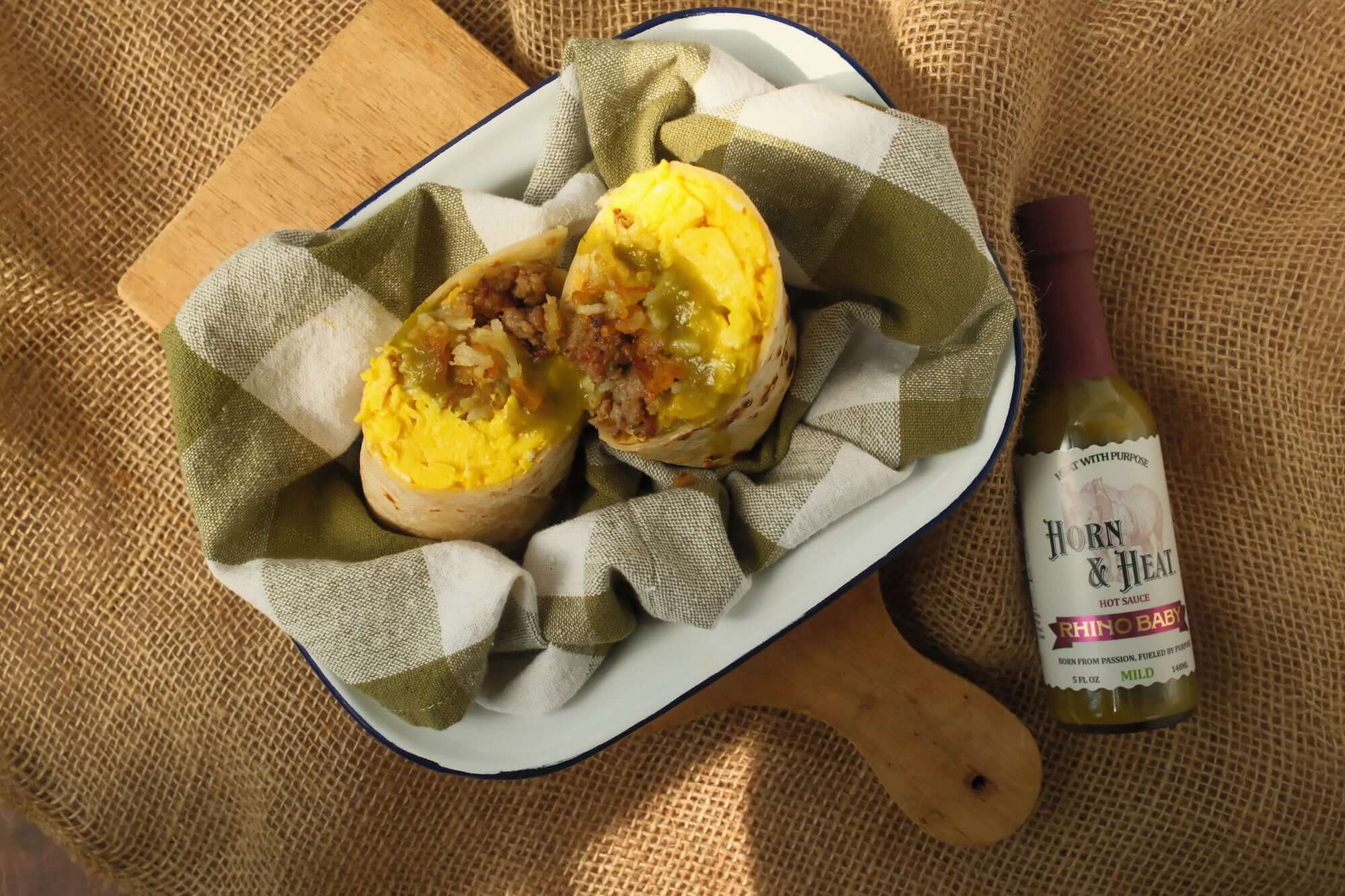 Horn & Heat Baby Rhino Breakfast Burrito served with green and white checkered cloth and a bottle of Horn & Heat sauce.