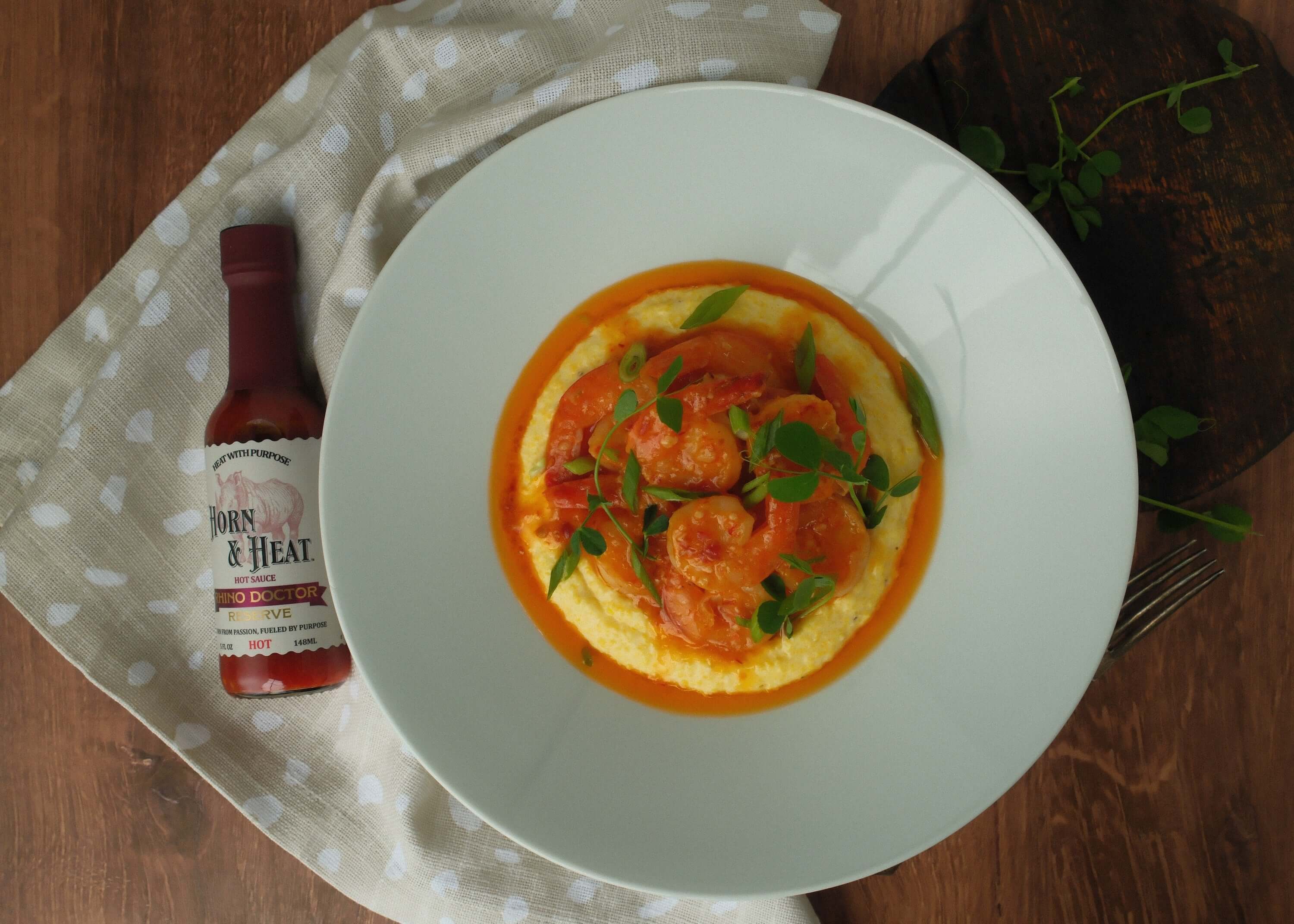 Rhino Doctor Reserve Butter Shrimp with Creamy Cheddar Polenta served with a bottle of hot sauce on a plate.