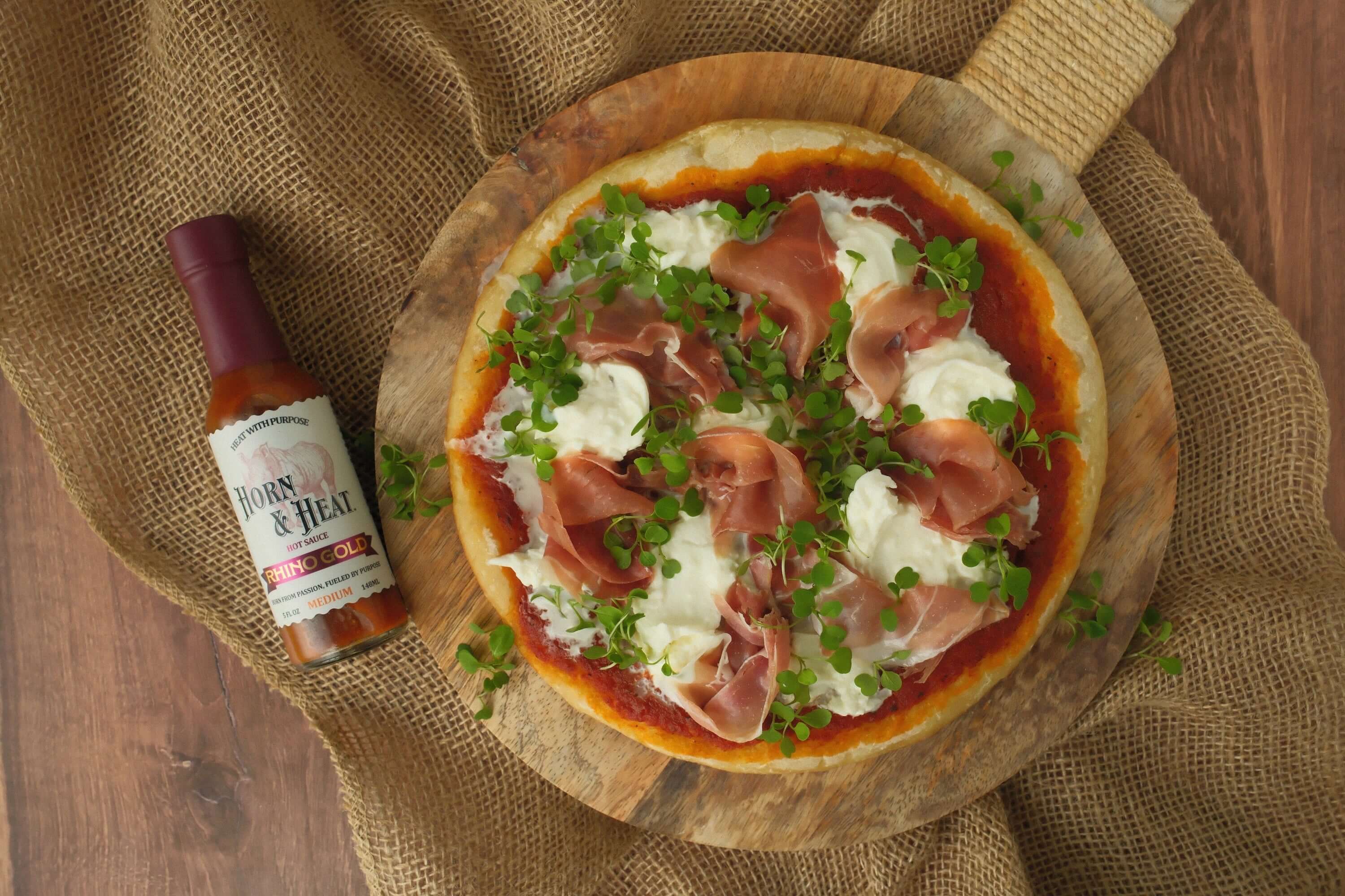 Horn & Heat Prosciutto & Burrata Pizza with Rhino Gold Sauce on a wooden board.
